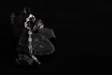 Photo of Luxury jewelry. Stylish presentation of elegant bracelet on coal against black background, space for text