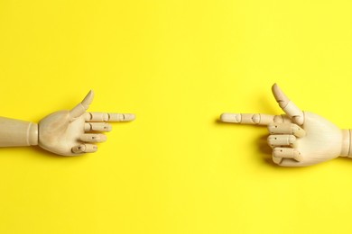 Wooden mannequin hands on yellow background, flat lay