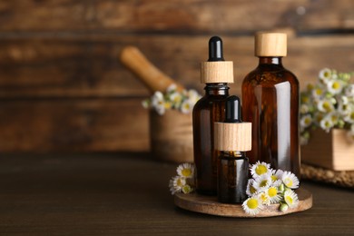 Bottles of chamomile essential oil and flowers on wooden table, space for text