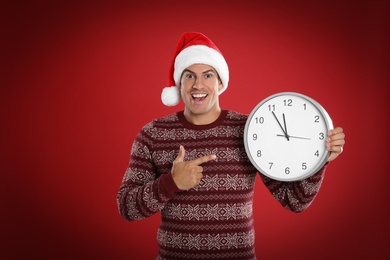 Man in Santa hat with clock on red background. New Year countdown