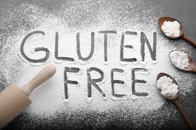 Words Gluten free written with flour and different kitchen utensils on grey background, flat lay