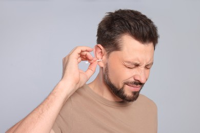 Photo of Man cleaning ears and suffering from pain on grey background