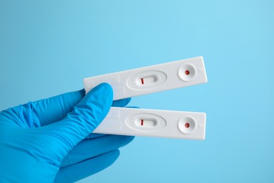 Doctor holding two disposable express tests for hepatitis on light blue background, closeup