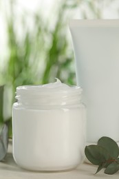 Different hand care cosmetic products and eucalyptus branches on white wooden table, closeup