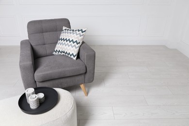 Stylish grey armchair and pouf with candles in room. Interior design
