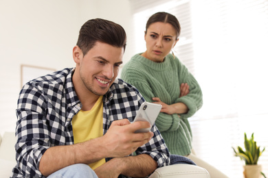 Distrustful woman peering into boyfriend's smartphone at home. Jealousy in relationship