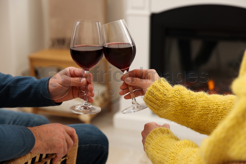 Photo of Lovely couple with glasses of wine spending time together near fireplace at home, closeup