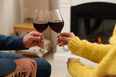 Photo of Lovely couple with glasses of wine spending time together near fireplace at home, closeup