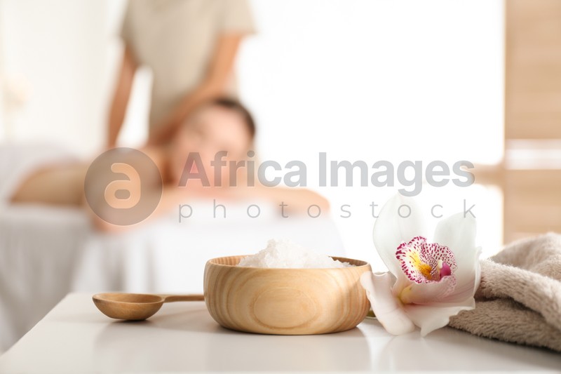 Photo of Bowl with sea salt and orchid flower on white table in spa salon. Space for text