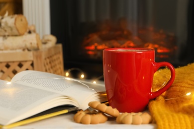 Cup of drink, book and cookies on table near fireplace
