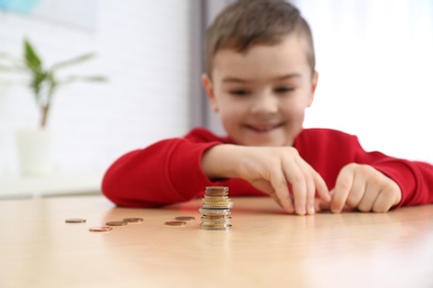Photo of Cute little boy with coins at home, closeup. Counting money
