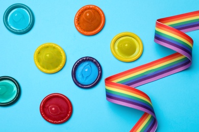 Colorful condoms and rainbow ribbon on light blue background, flat lay. LGBT concept