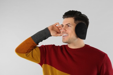Man wearing stylish earmuffs on light background