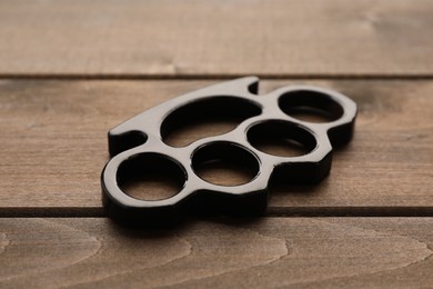 Black brass knuckles on wooden background, closeup