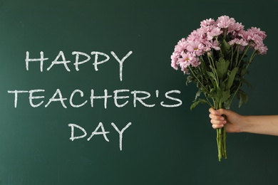 Girl holding beautiful bouquet near green chalkboard with text Happy Teacher's Day, closeup