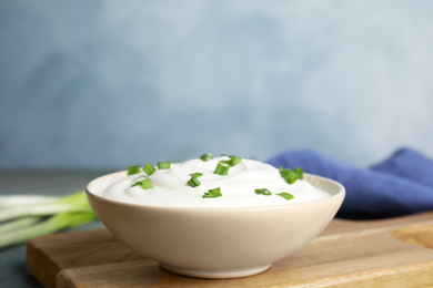 Fresh sour cream with onion on wooden board against light blue background, closeup