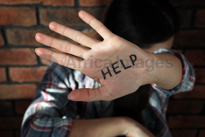 Photo of Domestic violence concept. Unhappy woman near brick wall, focus on hand with written word Help