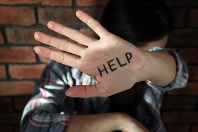Domestic violence concept. Unhappy woman near brick wall, focus on hand with written word Help