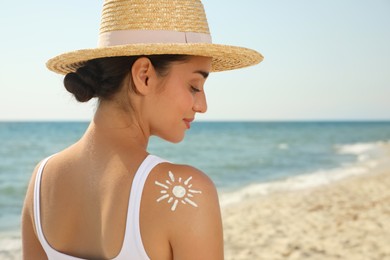 Beautiful young woman with sun protection cream on shoulder at beach