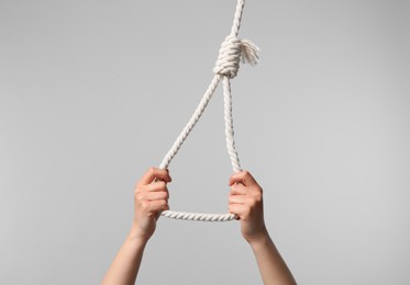 Woman holding rope noose on light grey background, closeup