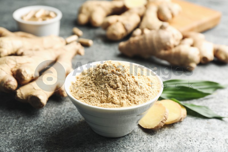 Dry ginger powder, fresh root and leaves on grey table