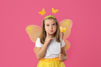 Cute little girl in fairy costume with yellow wings and magic wand on pink background