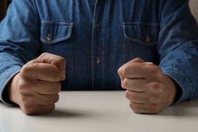 Photo of Man clenching fists at table while restraining anger, closeup