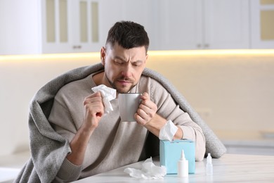 Ill man at table with nasal spray, drops and box of paper tissues in kitchen
