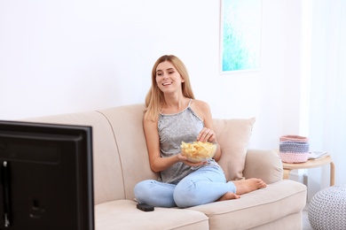 Photo of Woman with bowl of potato chips watching TV on sofa in living room