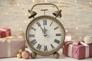 Vintage alarm clock with decor on white table against blurred Christmas lights, closeup. New Year countdown