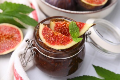 Photo of Glass jar of tasty sweet fig jam and fruits on table, closeup