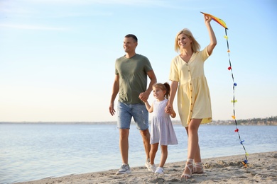 Photo of Happy parents with their child playing with kite on beach, space for text. Spending time in nature