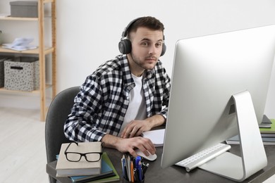 Young man in headphones using modern computer for studying at home. Distance learning