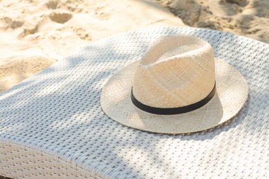 Photo of Sunbed with stylish straw hat on sandy beach, space for text