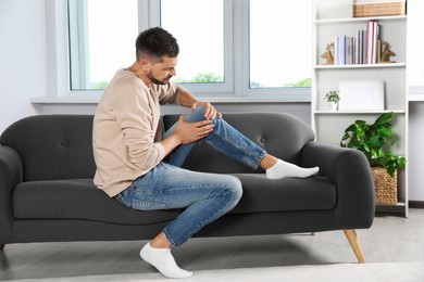 Man suffering from knee pain on sofa at home