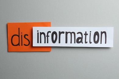 Word DISINFORMATION made with paper pieces on light grey background, flat lay
