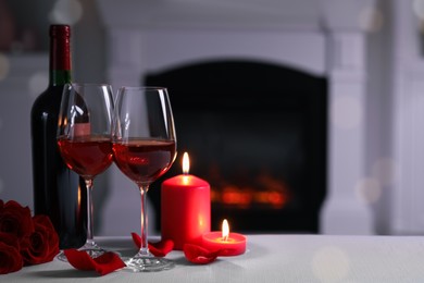 Photo of Glasses of red wine, burning candles and rose flowers on grey table indoors, space for text. Romantic atmosphere
