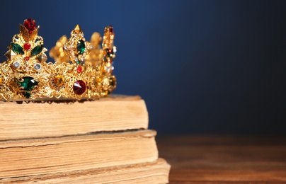 Beautiful golden crown on old books against dark blue background, space for text. Fantasy item