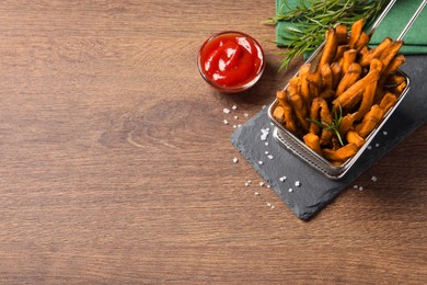 Frying basket with sweet potato fries and ketchup on wooden table, above view. Space for text