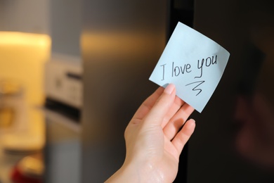 Woman with sticky note saying I Love You near fridge door, closeup. Romantic message