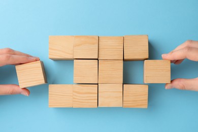 People holding wooden cubes near others on light blue background, top view. Management concept