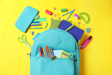 Stylish backpack with different school stationery on yellow background, flat lay