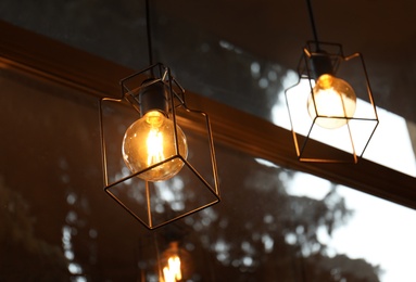 Pendant lamps with glowing light bulbs near window indoors