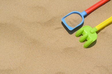 Plastic shovel and rake on sand, space for text. Beach toys