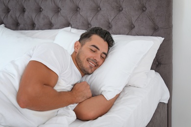 Photo of Young man sleeping in bed with soft pillows at home