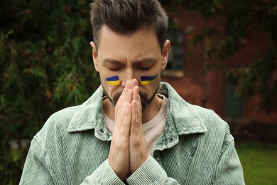 Photo of Sad man with drawings of Ukrainian flag on face outdoors