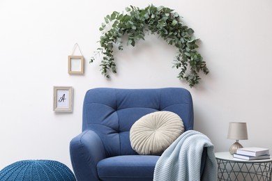 Stylish room decorated with beautiful eucalyptus garland above comfortable armchair