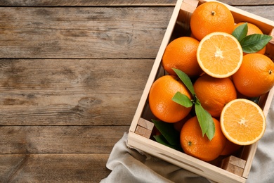 Delicious ripe oranges in crate on wooden table, top view. Space for text