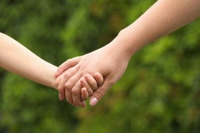 Woman and child holding hands outdoors, closeup