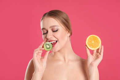 Photo of Young woman with cut kiwi and orange on pink background. Vitamin rich food